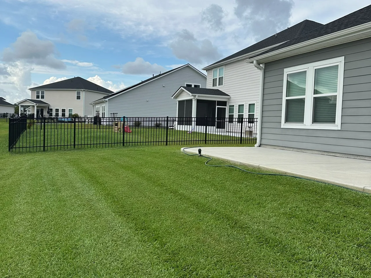 Fenced backyard with crisp mower stripes running the length of the lawn.