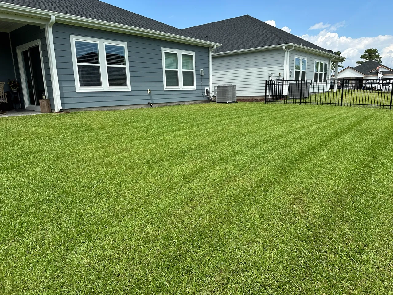 Freshly mowed backyard with sharp, even stripes behind a fenced home.