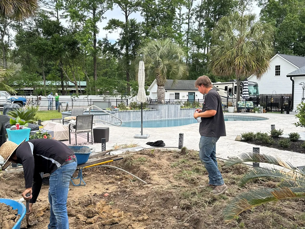 Two crew members preparing a planting bed beside a pool build.
