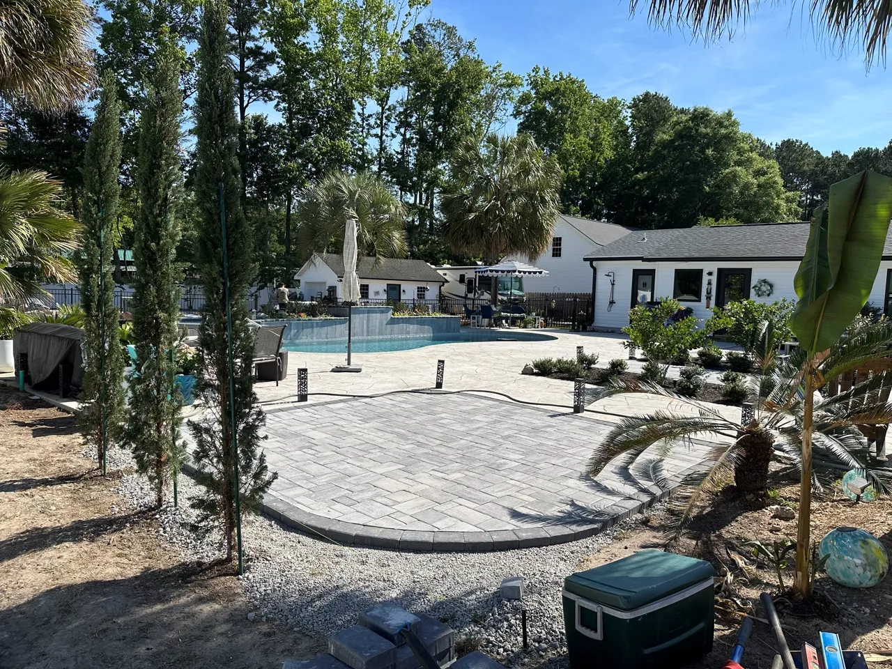 A circular paver patio being finished around a pool, crew still on site.