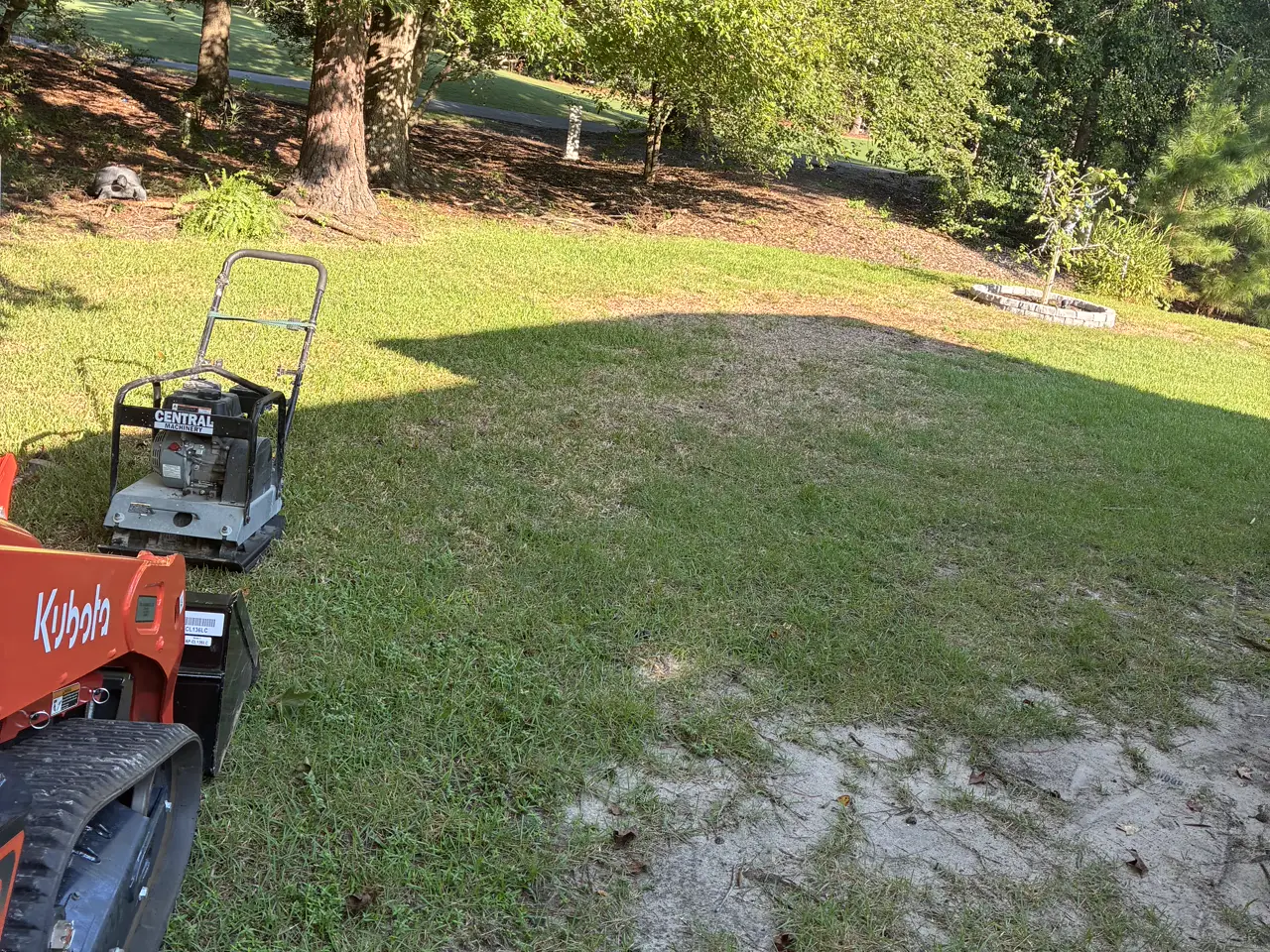 Track loader and plate compactor on site, the bare ground where a paver patio will go.