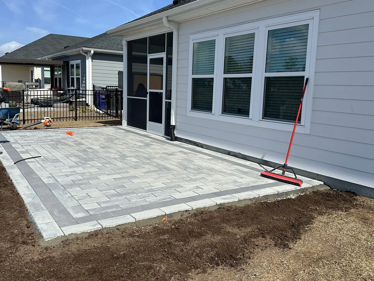 A paver patio mid-build: field laid, border set, soil ready for sod along the edge.