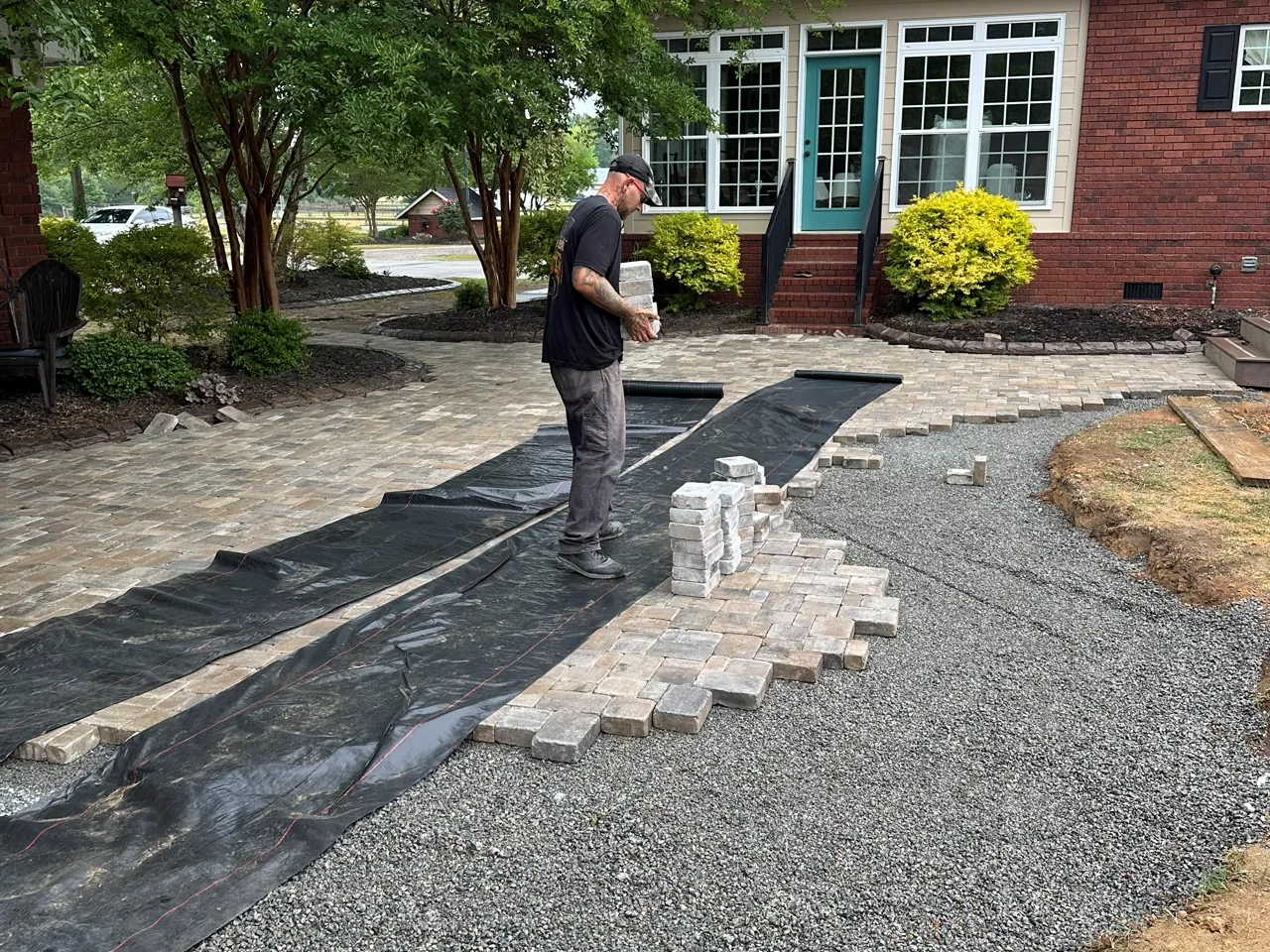 Crew member setting stone steps into a paver walkway, tools laid out on site.