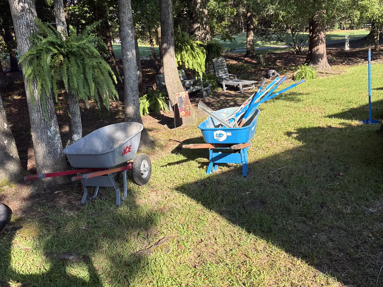 Wheelbarrows, rakes and tampers staged in the shade before a paver patio build.