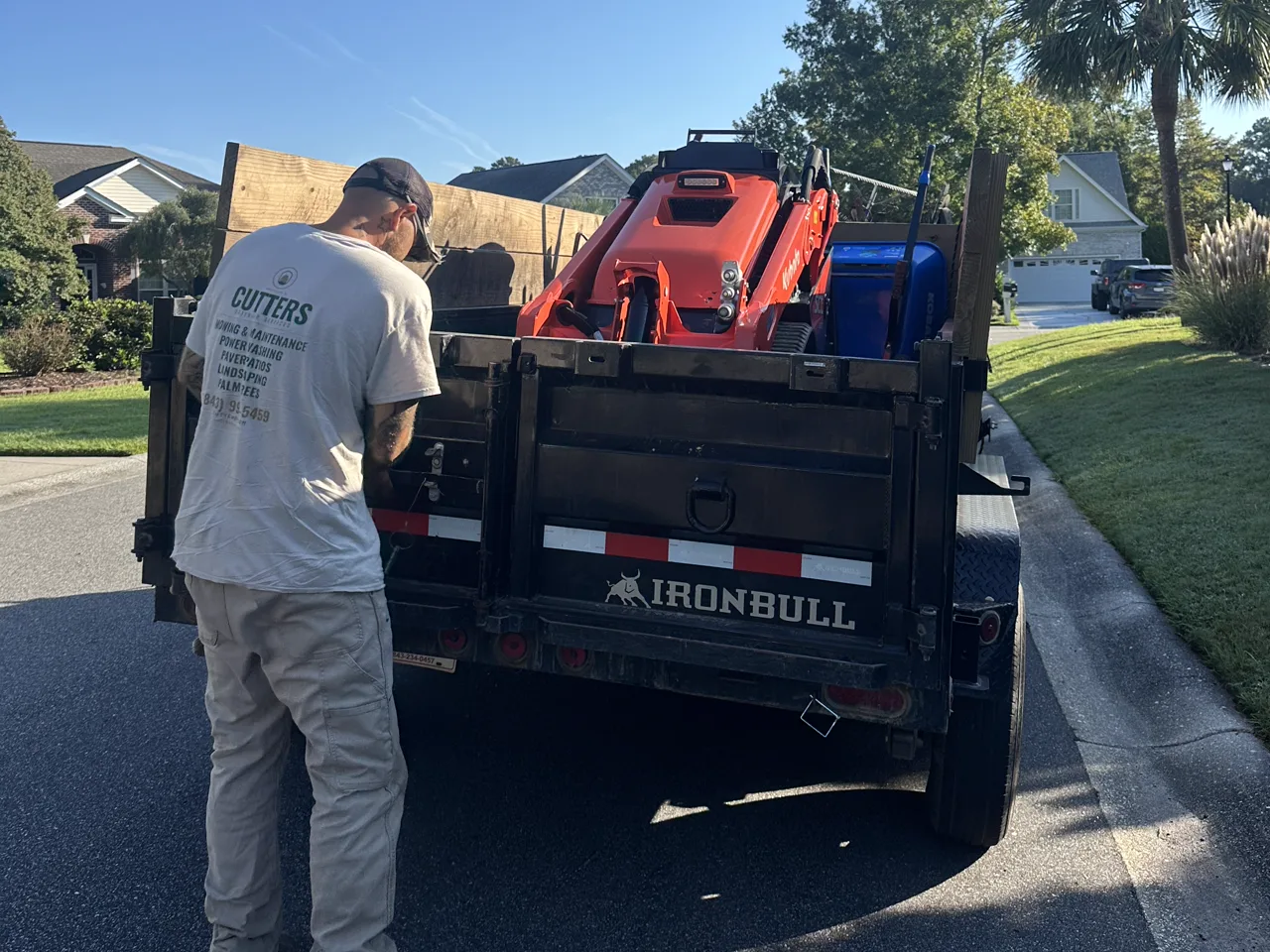 A Cutters crew member unloading a Kubota track loader from the dump trailer at the curb.