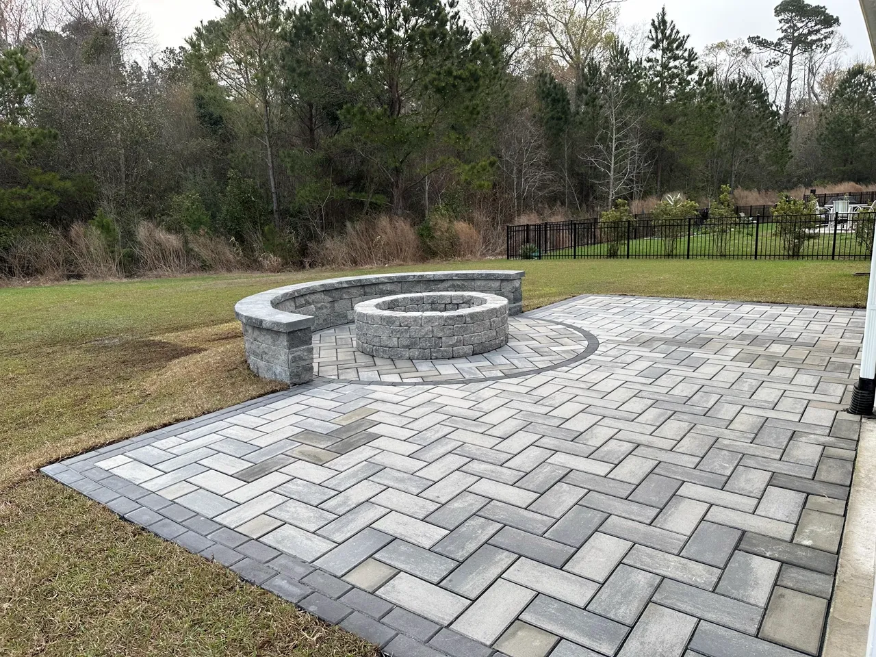 Herringbone paver patio with a built-in stone fire pit, backed by trees.
