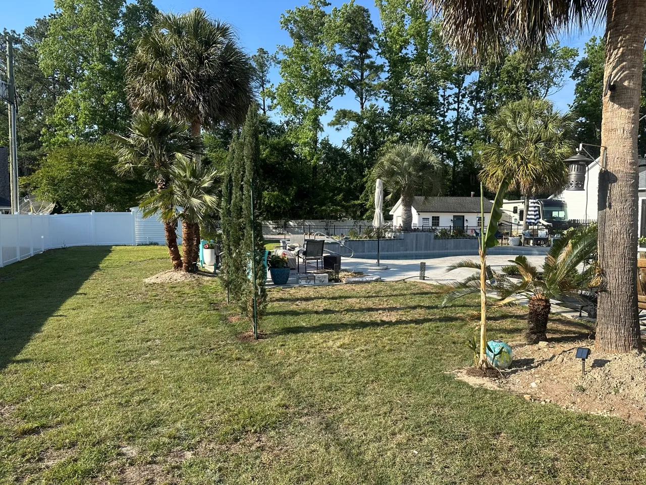 Paver path through tropical landscaping toward a fenced backyard pool.