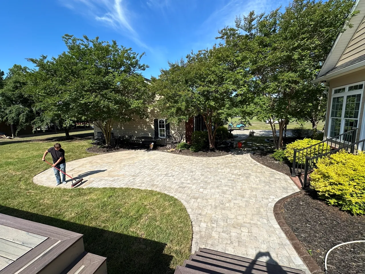 Curved paver patio wrapping a backyard, crew finishing the edge.