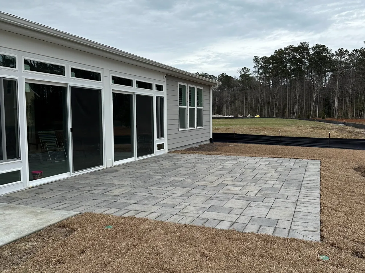 Finished paver patio across the back of a house, fresh mulch beds framing it.