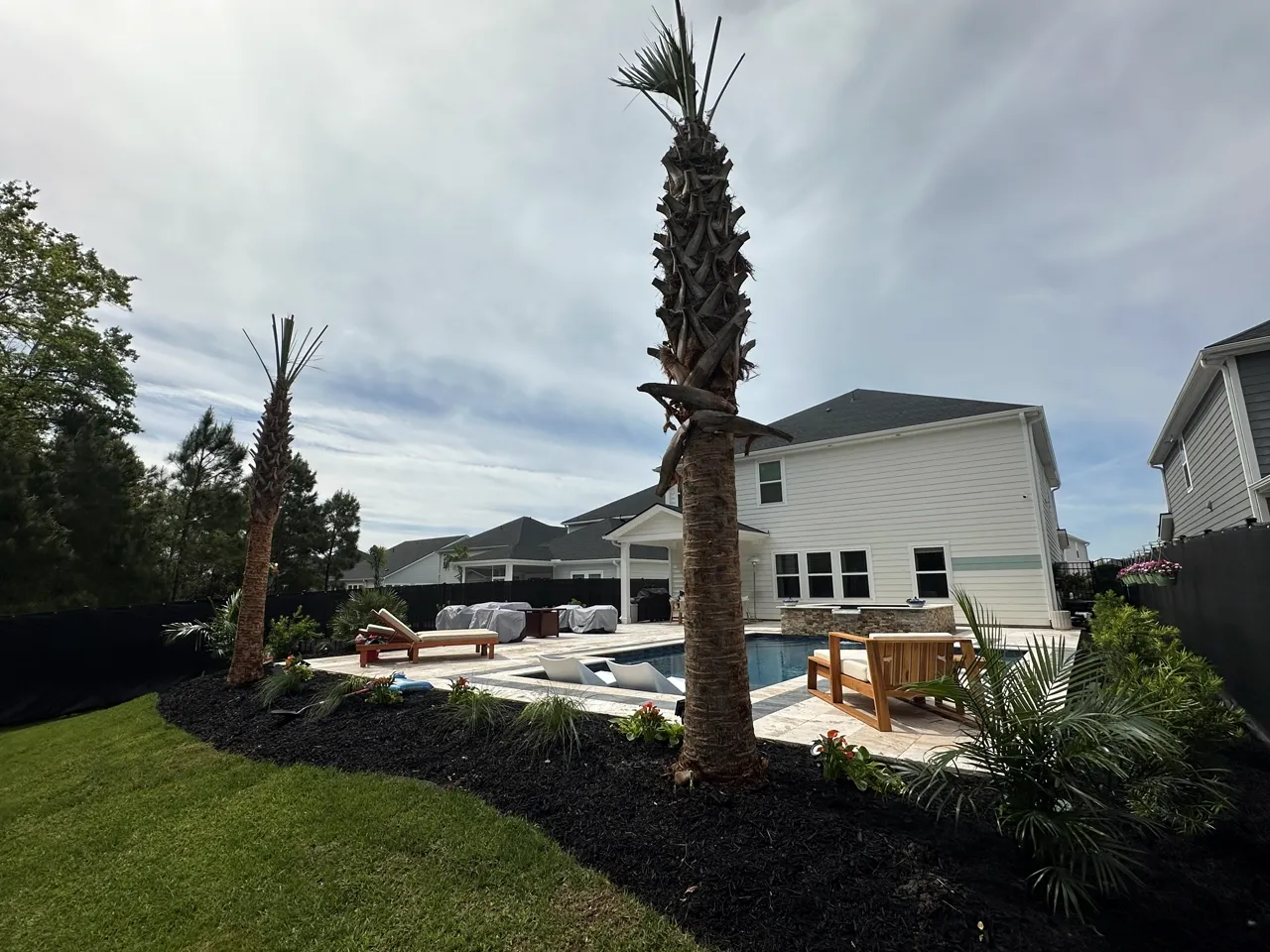 Finished paver pool deck with young palms and fresh landscaping around a new home.