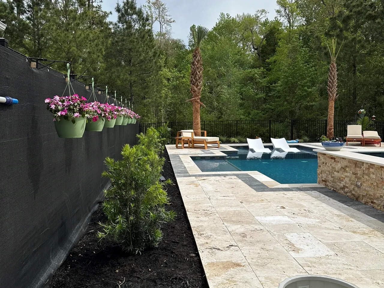 Travertine paver walkway running alongside a pool, planters and loungers set along the edge.