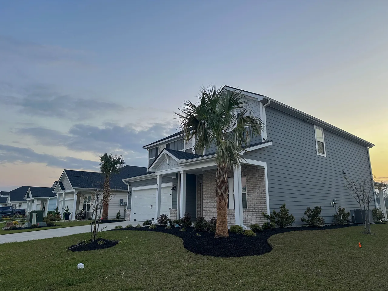 Cut lawn, fresh mulch beds, and trimmed palms at dusk in a Carolina Forest neighborhood.